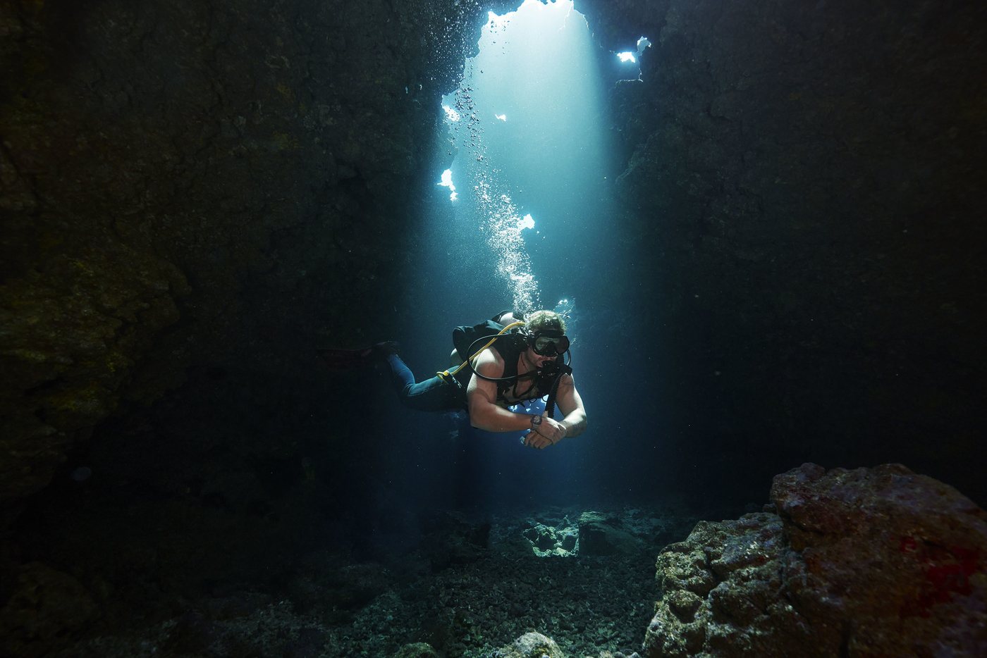 A diver hanging in shafts of light inside a sea cave