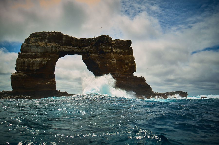 A wave breaking under a rock arch in open ocean