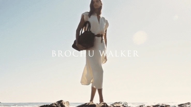 A woman in white on sunlit rocks above the sea, the brand name across the frame
