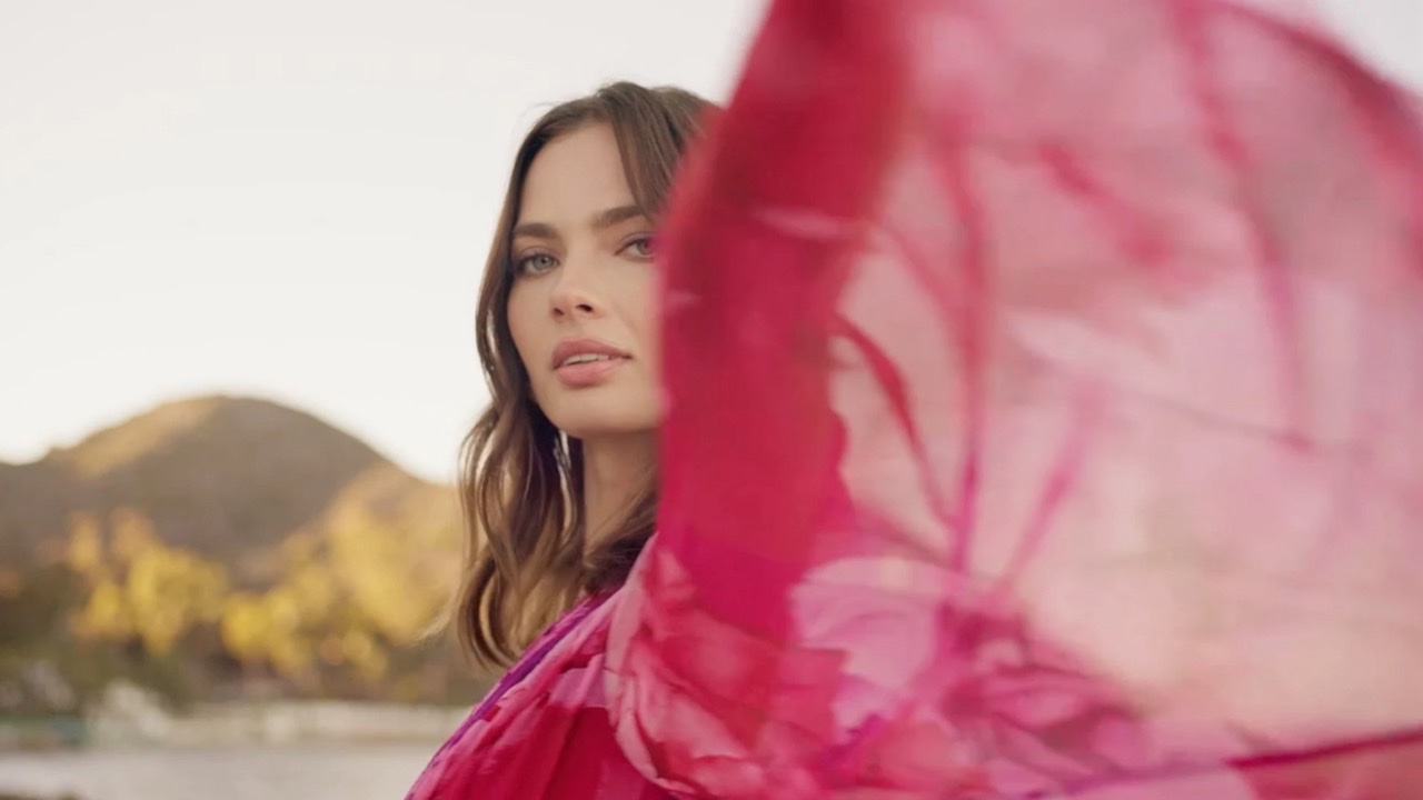 A woman turning as pink silk sweeps across the frame, hills behind her