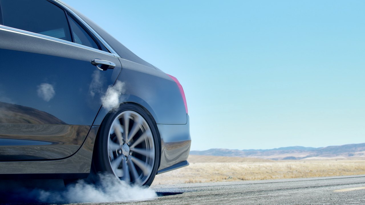 Cadillac CTS-V: a rear wheel spinning up smoke under a clear desert sky