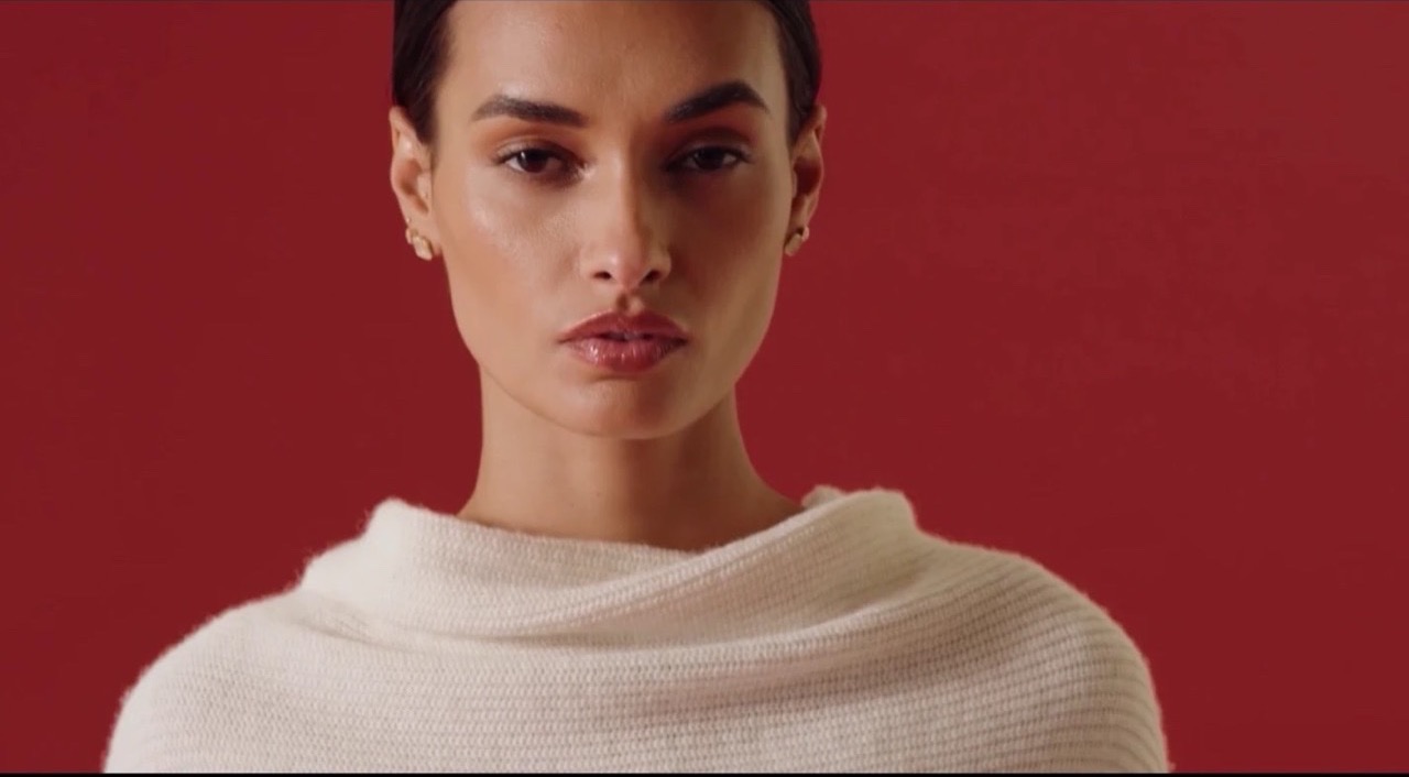 A model in a cream knit against a deep red backdrop