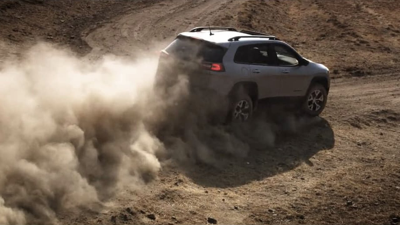 Jeep Cherokee throwing a wall of dust on a dirt climb