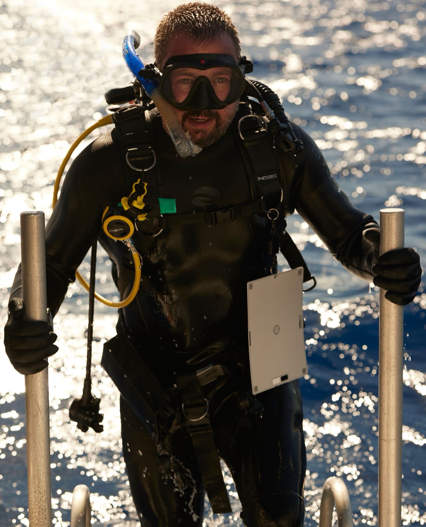 Jeffrey climbing a dive ladder in scuba gear, camera housing in hand, sun on the water