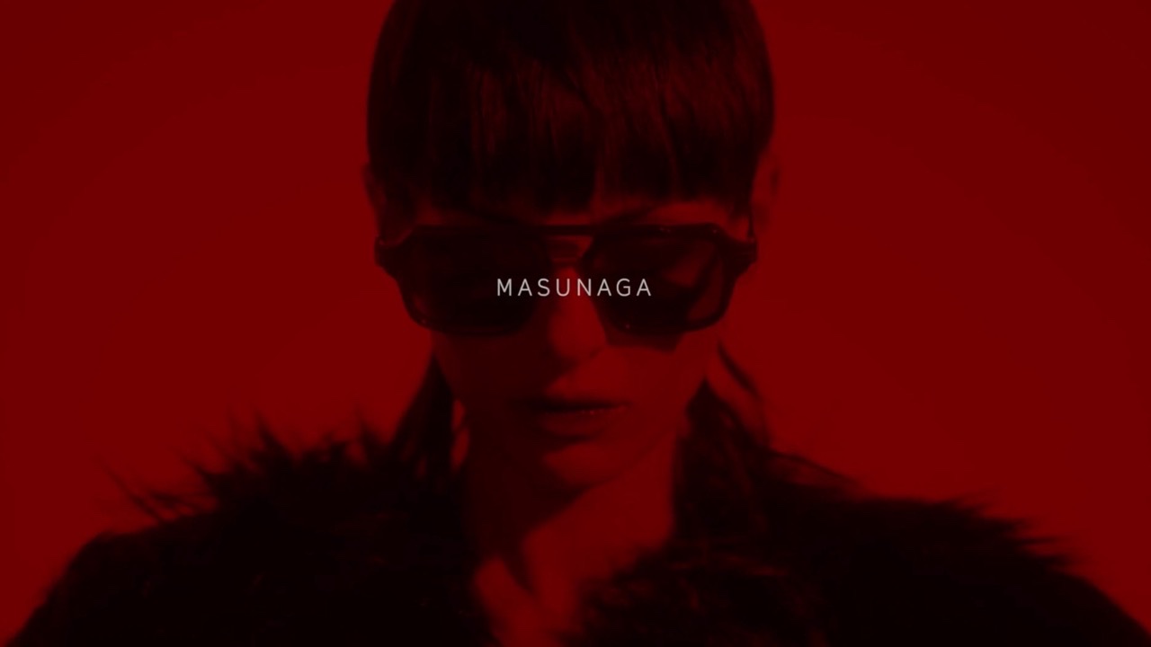 A woman in dark glasses under deep red light, the brand name across the frame
