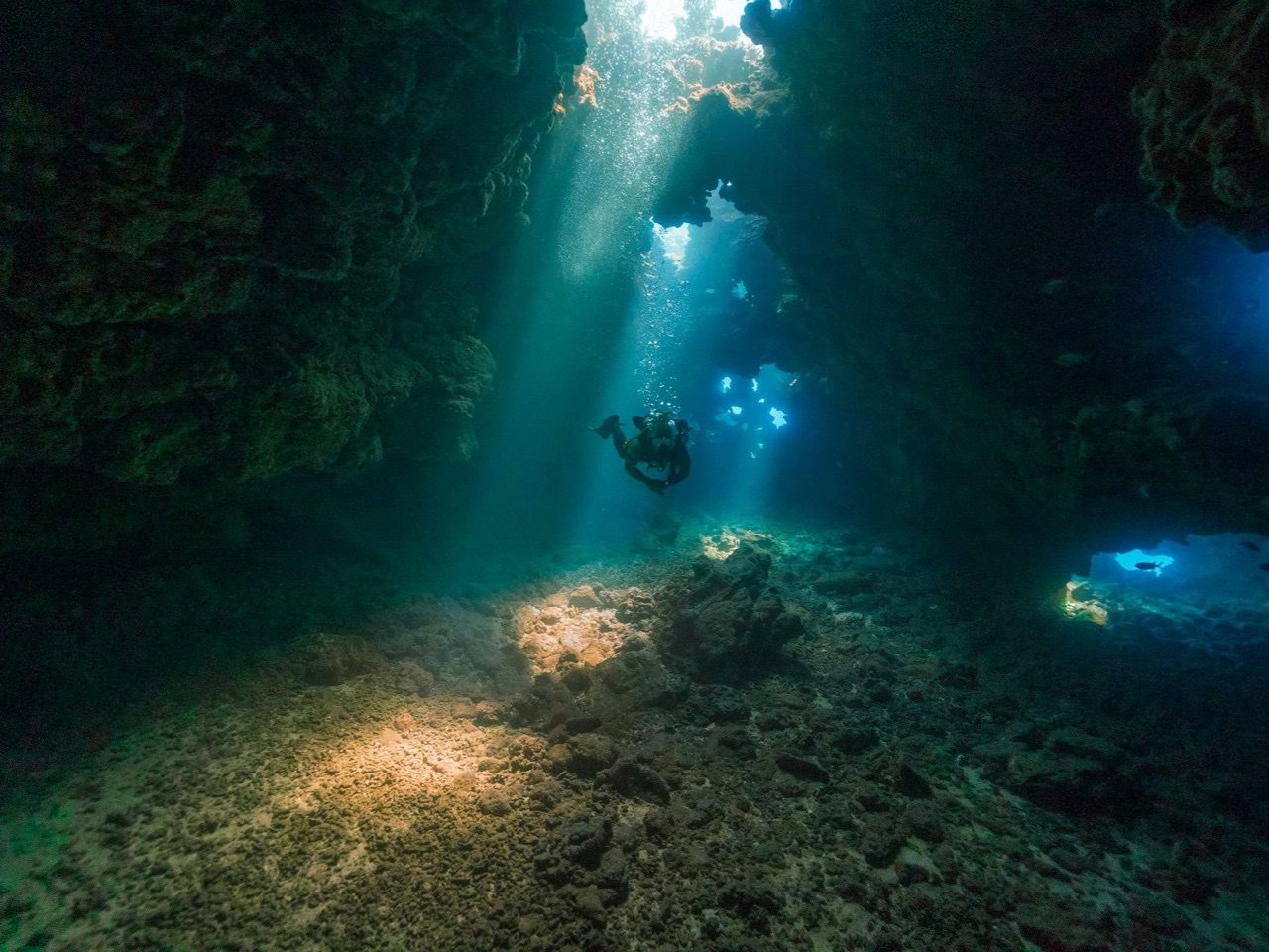 Shafts of light through the roof of a lava cave, a diver in the beam