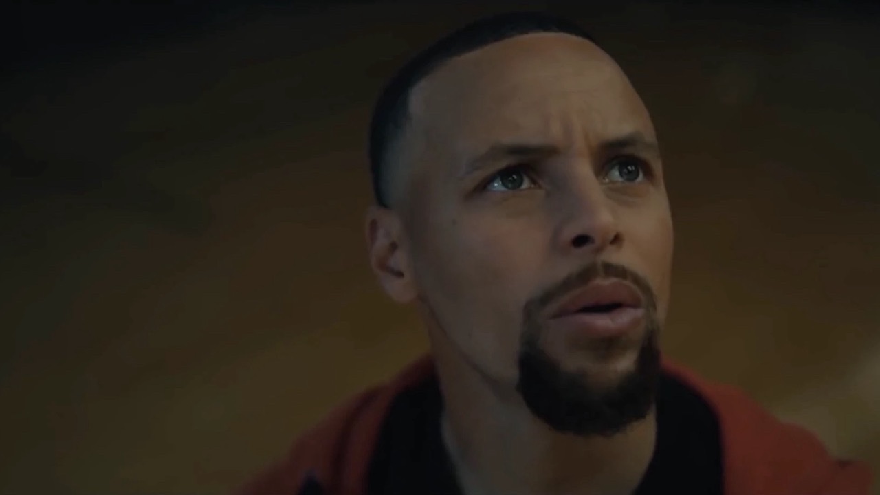 Steph Curry in close-up, looking up in a dark gym